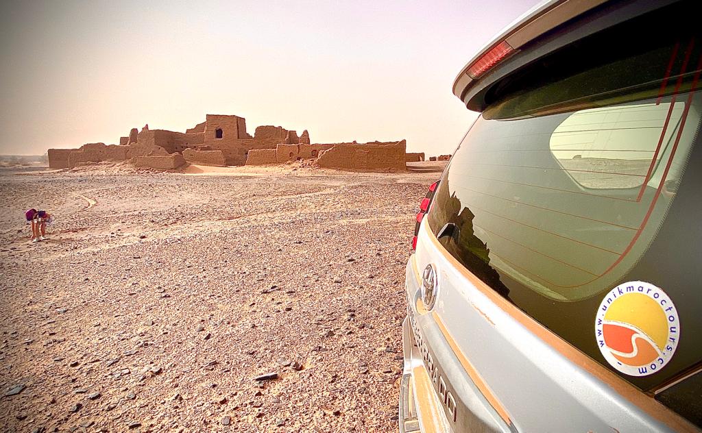 se ve la parte posterior de nuestro 4x4 toyota con el adhesivo de nuestro logo y al fondo la casa de adobe en ruinas del desierto de nuestro abuelo viajar a marruecos en noviembre unik maroc tours desierto desde marrakech